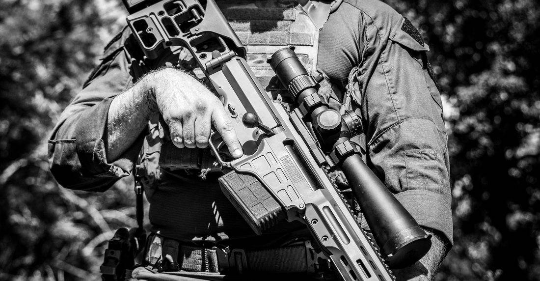 Tireur epaulant une Barrett MRAD equipee dune lunette et dun moderateur de son, boitier chargeur et crosse repliable visibles