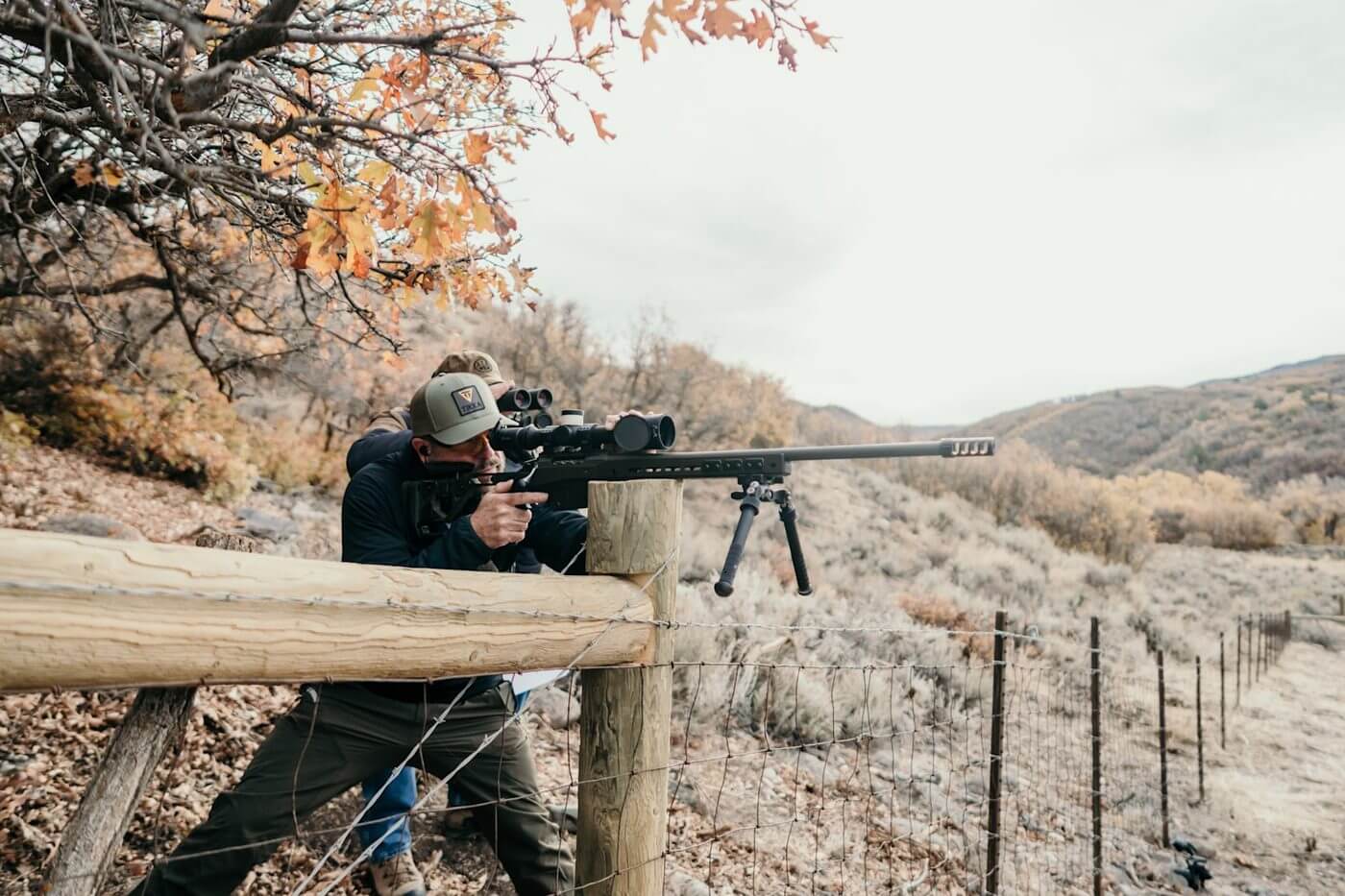 Tireur epaulant une Tikka T3x Ace Target noire avec bipied et frein de bouche en appui sur une barricade de bois