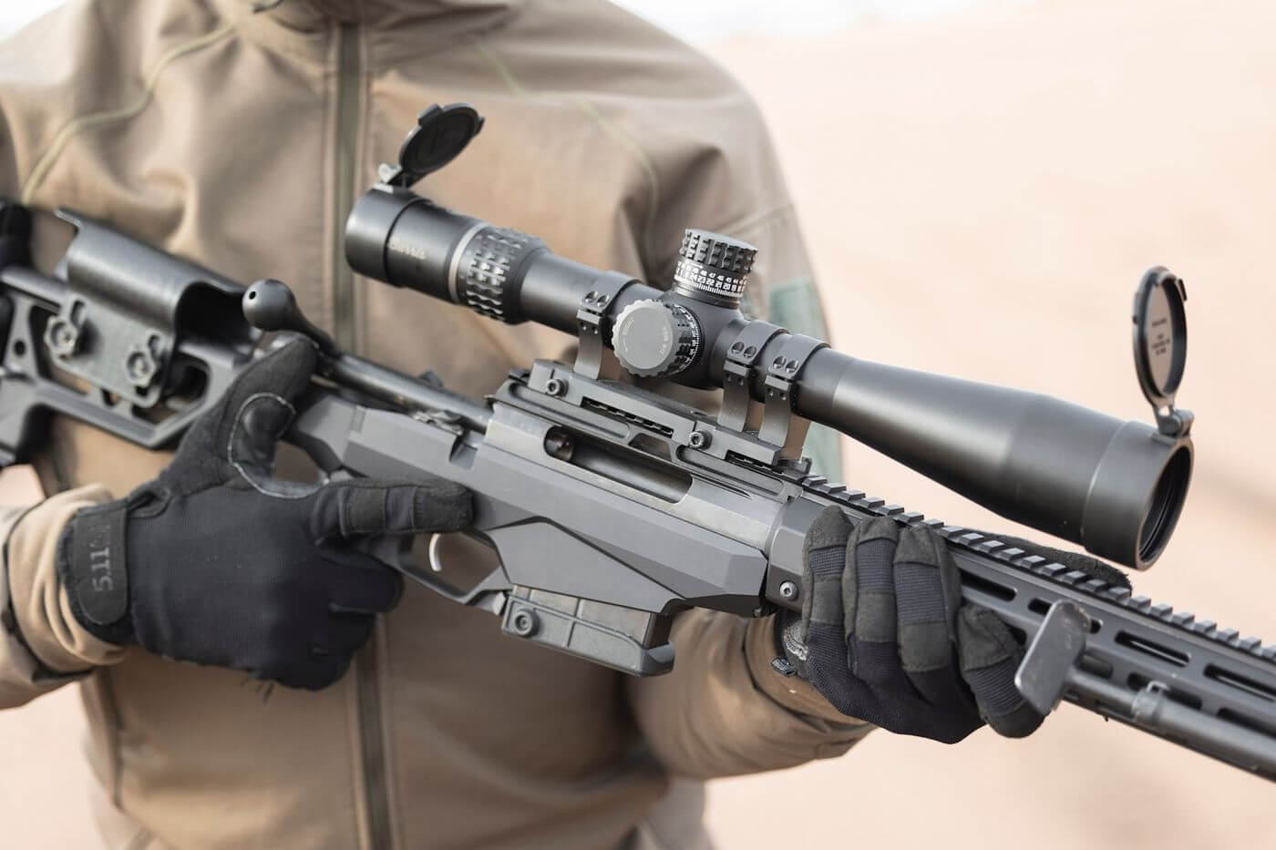 Tireur gante tenant une Tikka T3x TACT A1 crosse repliee contre le chassis avec lunette de tir montee